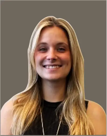 A person with long blonde hair smiles, wearing a sleeveless black top. The background is a solid gray color.