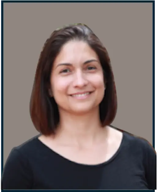 A person with shoulder-length hair is smiling and wearing a black top against a plain gray background.